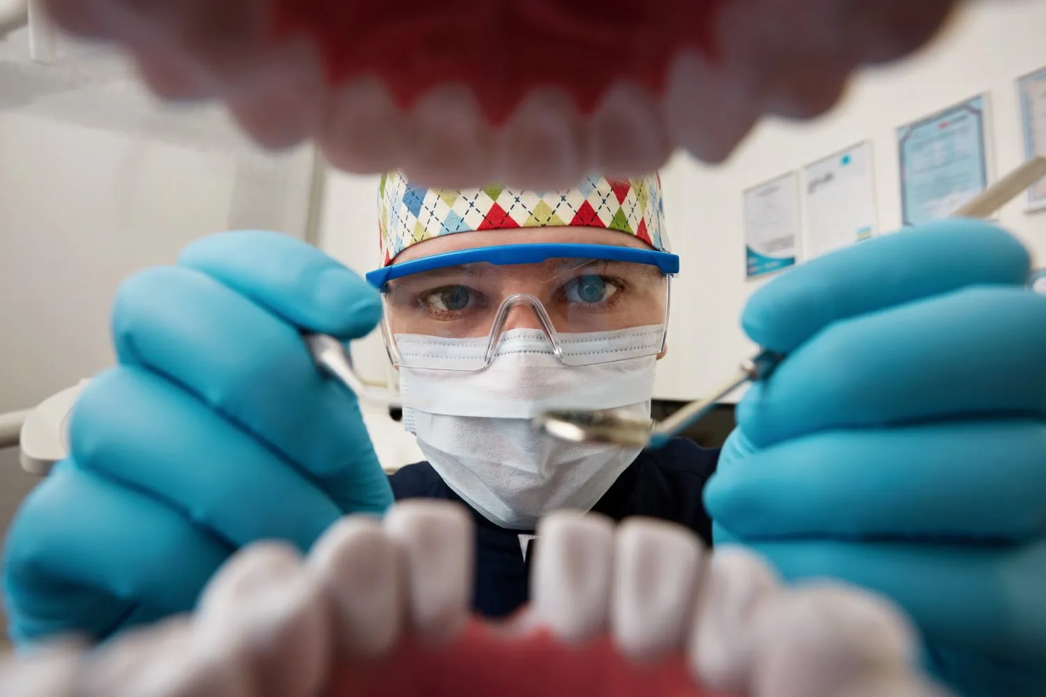 Dentista con mascarilla y gafas de protección visto desde la boca del paciente, con el instrumental en las manos