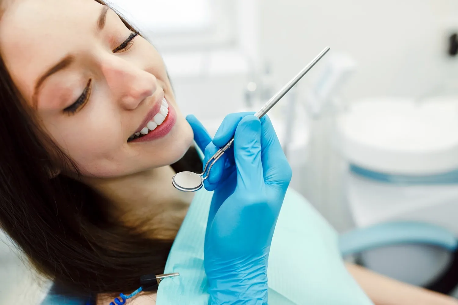 Paciente joven sonriente y relajada mientras el dentista revisa su boca con un espejo dental